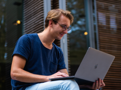 Ein Student sitzt mit einem Laptop auf einer Treppe.